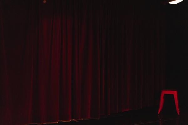 Photo d'une scène de théâtre avec les rideaux rouge et un tabouret rouge